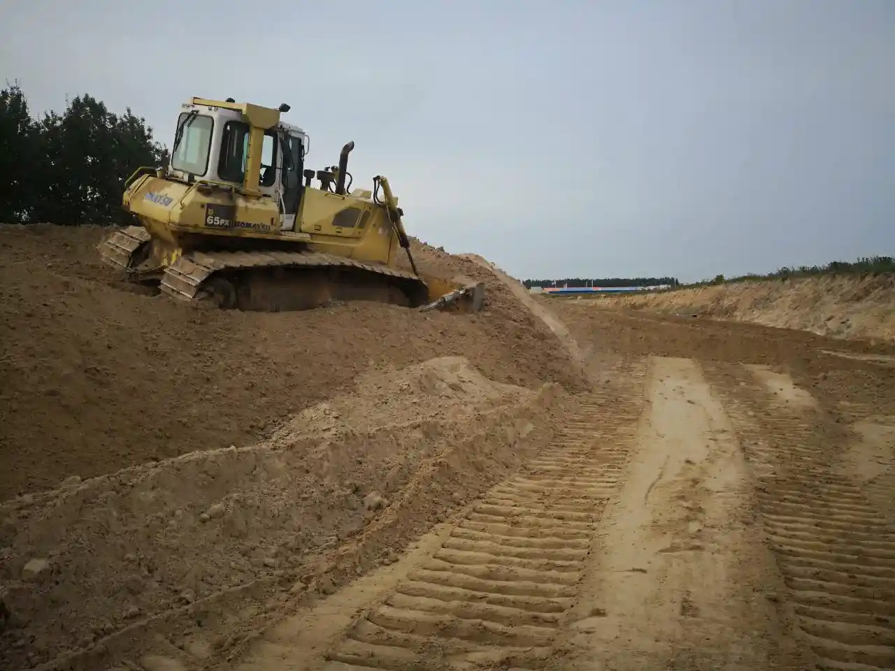 Бульдозер выполняет планировку территории — выравнивание песчаного основания и формирование откосов на строительной площадке.