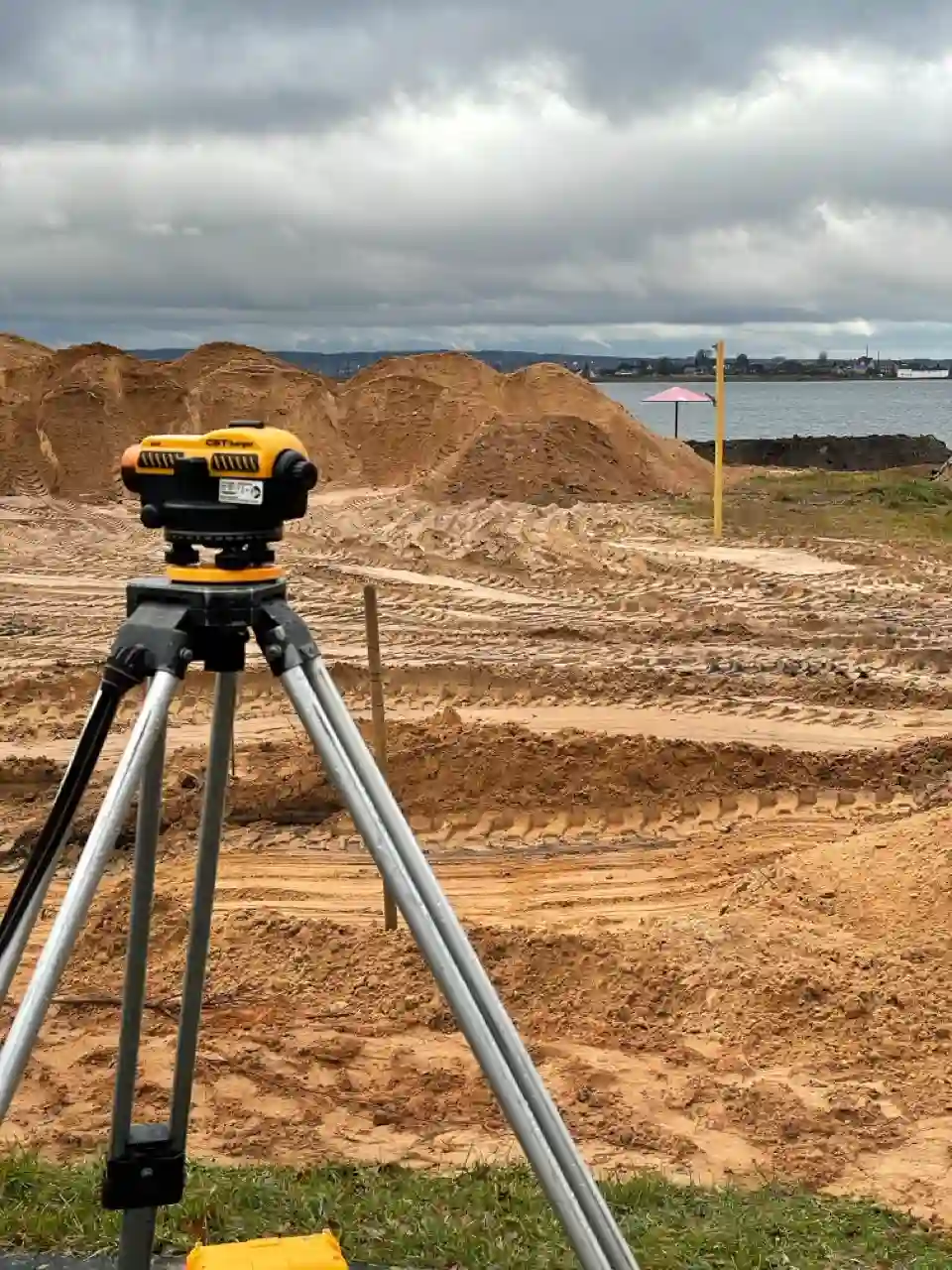 Нивелир на штативе на объекте планировки территории у озера в Смолевичах — контроль отметок и уклонов.